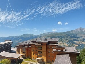 Ein mehrstöckiges Gebäude mit Holzfassade und geneigtem Dach, umgeben von Bergen und blauem Himmel.