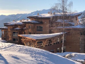 A multi-story building with a wooden facade and snow-covered roofs, set against a mountainous backdrop. - Spacious and quiet duplex - 12 guests (Les Arcs 1800)