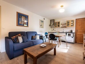 A living room with a sofa, a coffee table, and a dining area with chairs and a table. - Charming chalet, parking - 4 guests (Bozel)