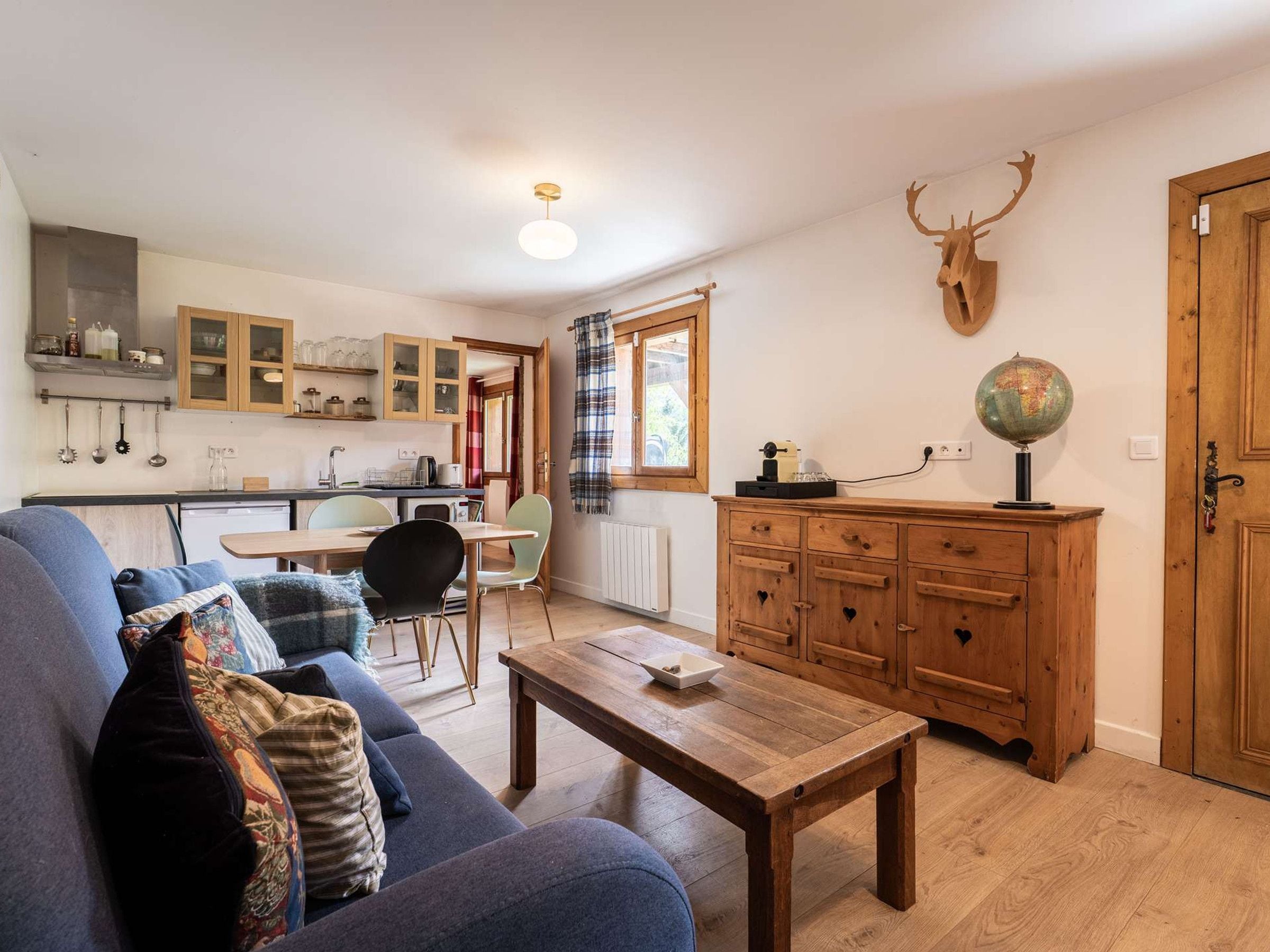 A cozy living room with a sofa, a wooden coffee table, and a kitchen area with cabinets and a window.