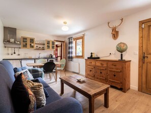 A cozy living room with a sofa, a wooden coffee table, and a kitchen area with cabinets and a window. - Charming chalet, parking - 4 guests (Bozel)