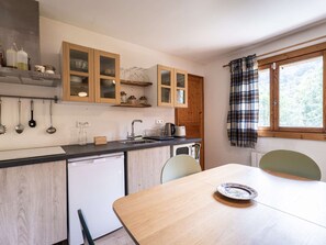 A compact kitchen with wooden cabinets, a sink, and a dining table with a plate. - Charming chalet, parking - 4 guests (Bozel)