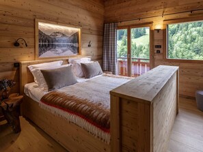 Quarto de cabana de madeira com uma cama, janela com vista para uma floresta e uma imagem pendurada na parede.