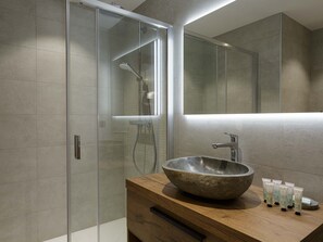Ein modernes Badezimmer mit einer gläsernen Dusche, einem hölzernen Waschtisch mit großem Becken und einem Spiegel darüber.