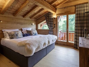 A wooden cabin bedroom with a large bed, plaid curtains, and a view of the outdoors. - Luxurious 5-Star Chalet in Morzine - Sleeps 12, Jacuzzi, Sauna, Near Ski Lift (Morzine)