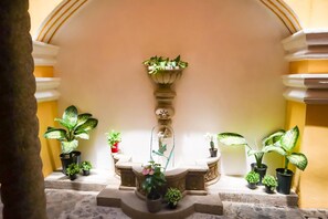 Une cour intérieure avec une fontaine centrale, entourée de plantes en pot.