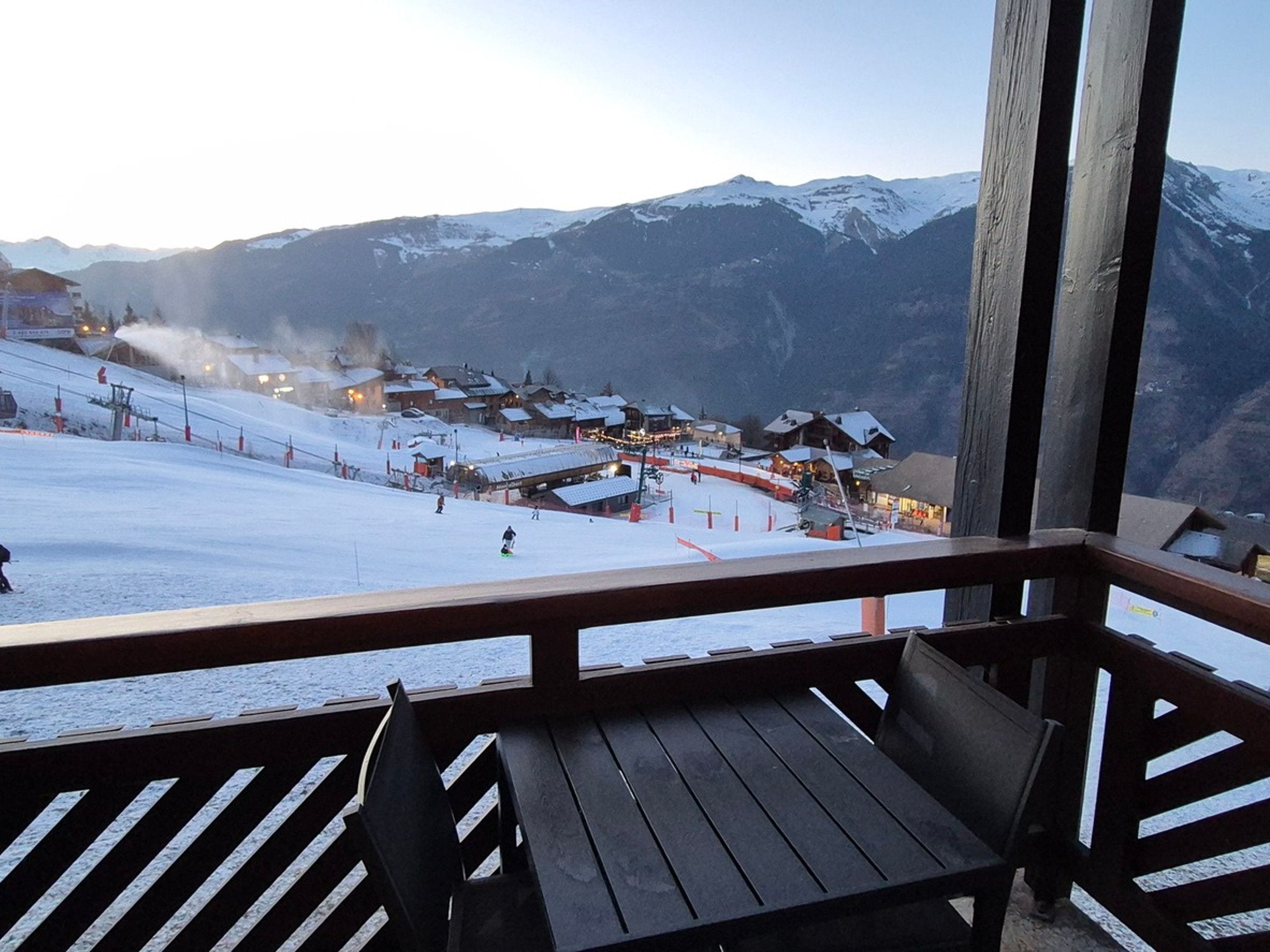A wooden deck with a view of a snow-covered ski slope and mountain range.