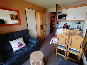 Un espacio habitable compacto con sofá, una pequeña mesa redonda, zona de comedor con sillas, cocina con armarios y un microondas.
