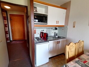 Una cocina funcional con armarios blancos, microondas, hervidor y pileta.