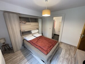 Un dormitorio con cama, armario, espejo y lámpara colgante.