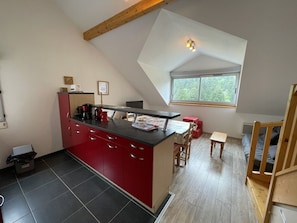 A modern kitchen with a red island, a dining area with a small table, and a window providing a view of greenery. - Duplex apartment with parking - 6 guests (Le Lioran)