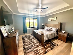 Une chambre à coucher comprenant un lit, des tables de chevet, une commode, un ventilateur de plafond et une fenêtre avec des rideaux.