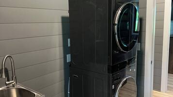 A compact laundry area with a washing machine and dryer stacked vertically, a stainless steel sink, and a wooden floor.