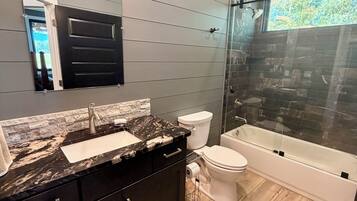 Ein modernes Badezimmer mit Marmorwaschtisch, Toilette, Badewanne und einer Duschkabine aus Glas.