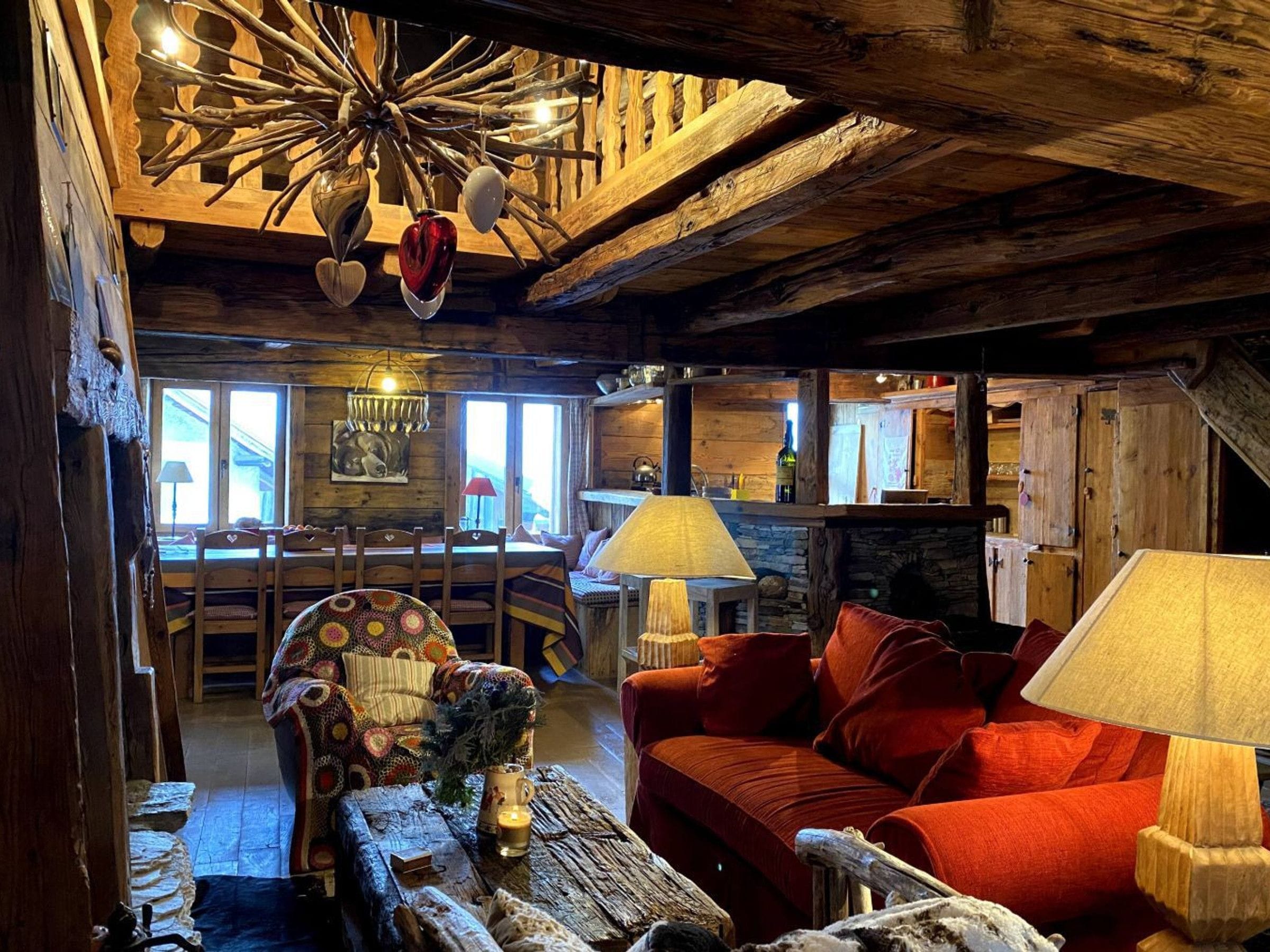 A rustic interior with a wooden ceiling, a dining area with a table and chairs, a red sofa, and a fireplace.