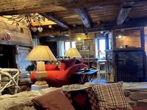 A rustic interior with a stone fireplace, wooden beams, and a red sofa. - Comfortable chalet - 12 guests (Tignes)