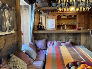 A cozy cabin interior with a wooden dining table, checkered cushions, and a variety of kitchen utensils hanging above. - Comfortable chalet - 12 guests (Tignes)
