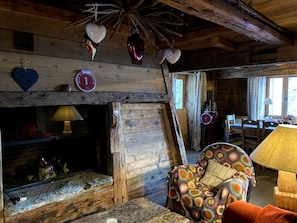 A rustic cabin interior with a wooden fireplace, a cozy seating area with a patterned armchair, and a dining table. - Comfortable chalet - 12 guests (Tignes)