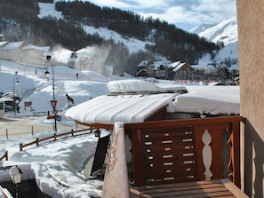 Ein mit Schnee bedeckter Balkon mit Holzgeländer mit Blick auf einen Skigebiet.