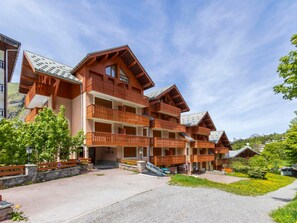 A multi-story wooden building with balconies, a gravel driveway, and a mountainous backdrop. - Peaceful apartment with parking - 4 guests (Valloire)