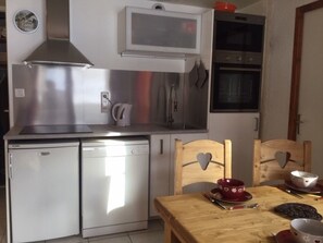 A compact kitchen with a stainless steel range, a dishwasher, and a microwave. There is a wooden dining table with chairs, and a red bowl on the table. - Peaceful apartment with parking - 4 guests (Valloire)