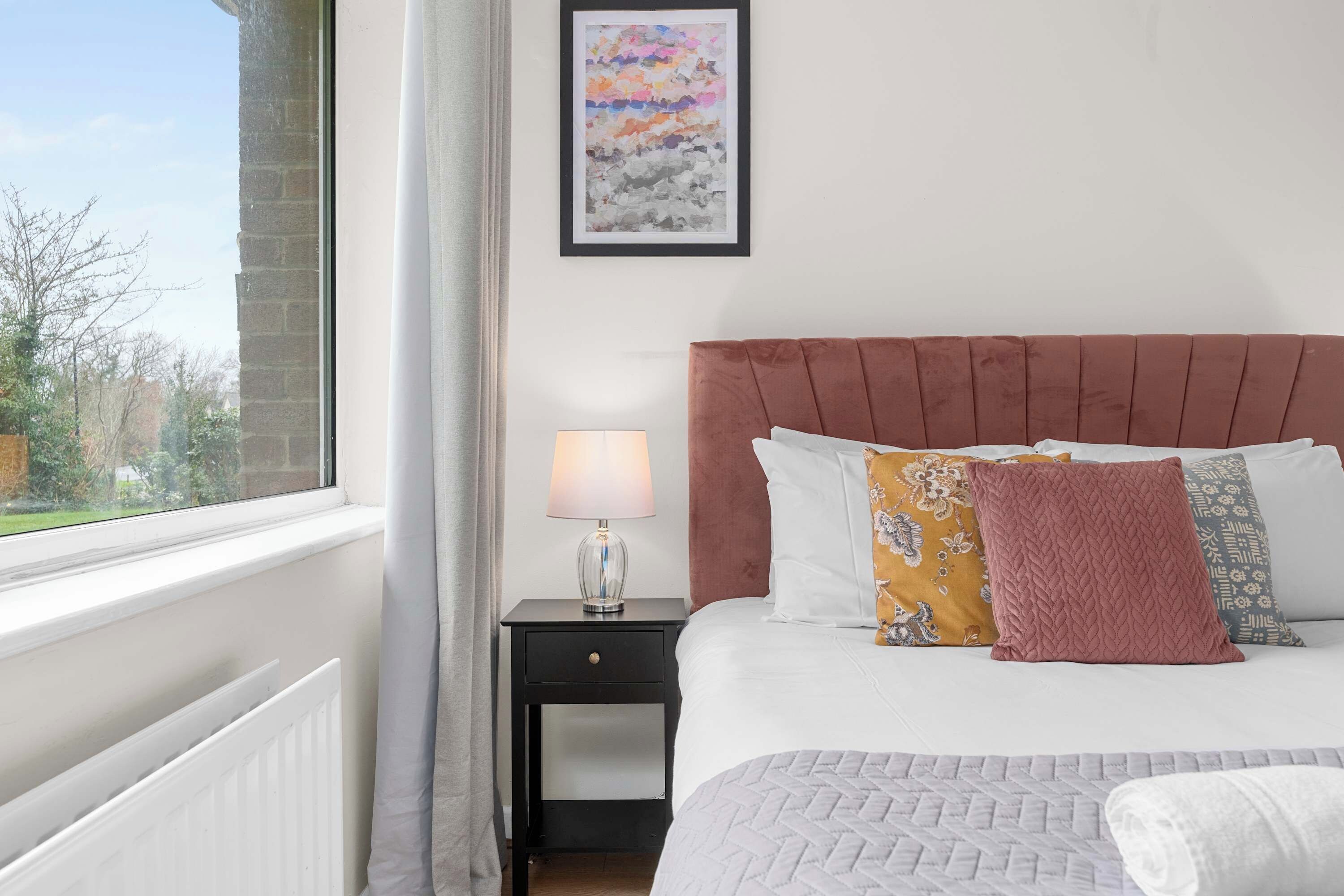 A bedroom with a bed, a nightstand, a lamp, and a window with a view.
