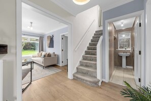 A modern interior with a staircase leading to a bathroom, a living area with a sofa and a coffee table, and a view of the outdoors. - Hale Barns Home - Garden, Parking & Near Airport (Hale)