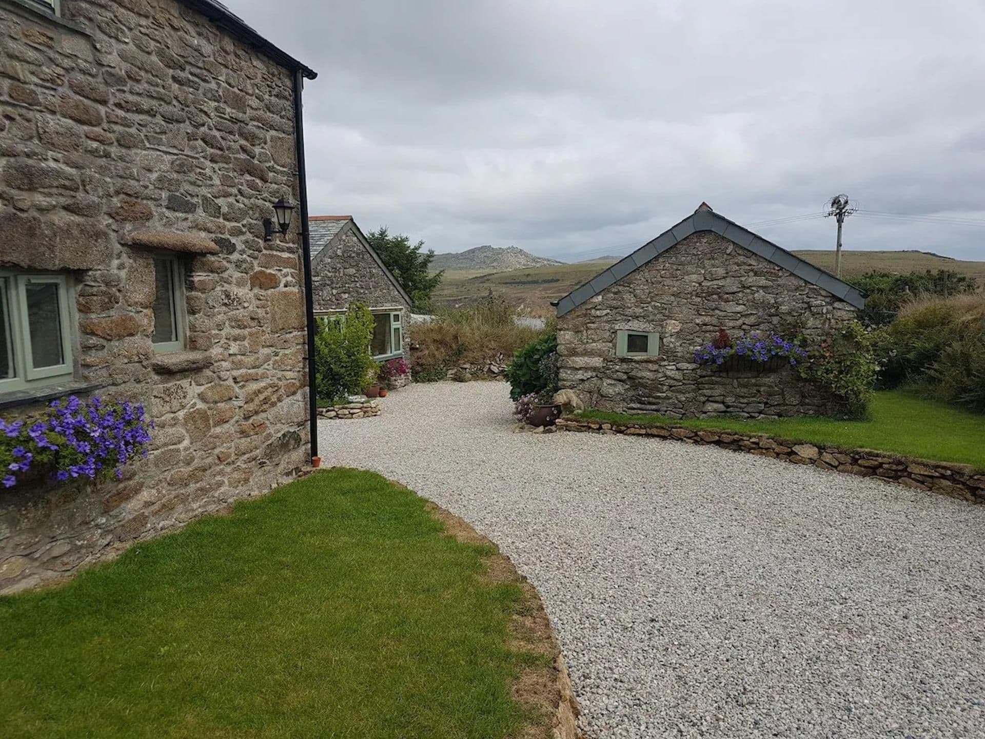 A stone building with a gravel driveway leading to a grassy area.