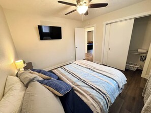 A bedroom with a bed, a ceiling fan, a TV mounted on the wall, and a door leading to a closet.