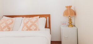 Ein ordentlich gemachtes Bett mit gemusterten Kissen, eine Nachttischlampe und ein Schild mit der Aufschrift 'LIVE LOVE LAKE'.