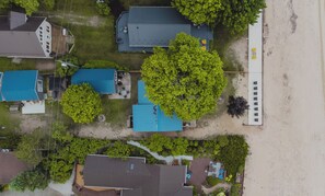 Ett flygbildsbild av ett bostadsområde med flera hus, några med blå tak, omgivet av grönska och en sandstrand.