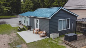 A small cabin with a blue roof, a patio with a table and chairs, and a large window. - The Driftwood Cottage - Lake Huron Access (Lambton Shores)