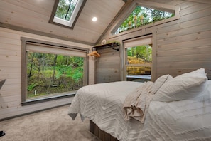 A bedroom with a large bed, two windows, and a skylight.