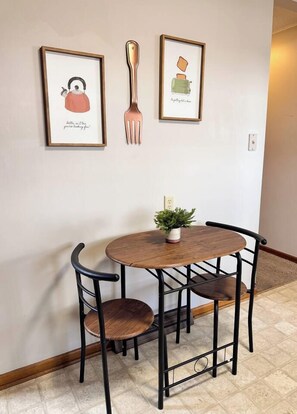A dining area with a round table, four chairs, and two framed artworks on the wall. - Serenity on Arthur Beatrice (Beatrice)