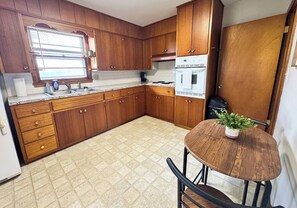 A kitchen with wooden cabinets, a countertop, a sink, a window, and a table with a plant. - Serenity on Arthur Beatrice (Beatrice)