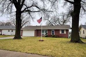 A residential area with a house featuring a brick facade, a white garage door, and a flagpole with an American flag.