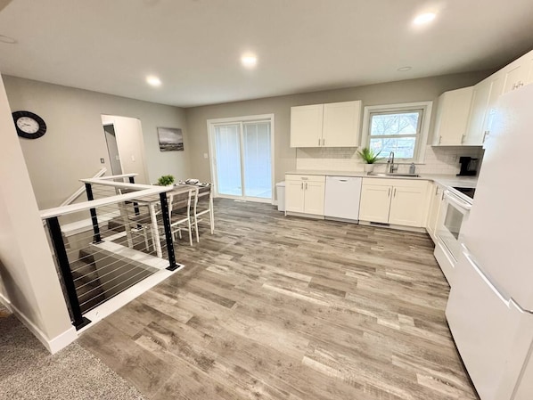 A modern kitchen with white cabinets, a stainless steel refrigerator, and a wooden floor.
