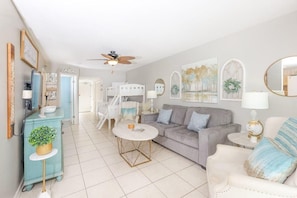 A living room with a sofa, a coffee table, a side table, a ceiling fan, and a decorative plant. - Phoenix East II 2092 (Orange Beach)