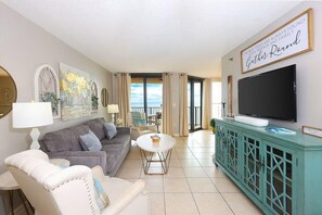 A living room with a grey sofa, white armchair, and a teal cabinet with a flat-screen TV. - Phoenix East II 2092 (Orange Beach)