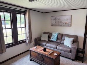 A living room with a brown leather sofa, a wooden coffee table, and a painting on the wall. - The Farm House at Sunnybrook Farms (Van Buren)