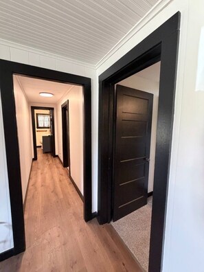 Un couloir doté d’un plancher en bois, de murs blancs et de portes à cadre noir.