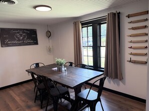 En matplats med ett träbord och stolar, en tavla där man kan skriva med krita och ett fönster med gardiner.