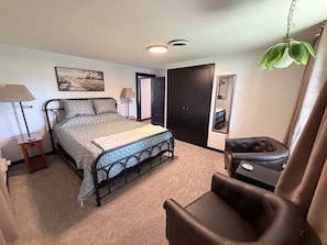 A bedroom with a bed, bedside table, lamp, chair, and a door. - The Farm House at Sunnybrook Farms (Van Buren)