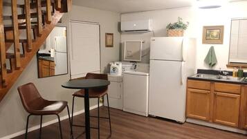 A compact kitchen with a dining area, wooden staircase, and a single refrigerator.