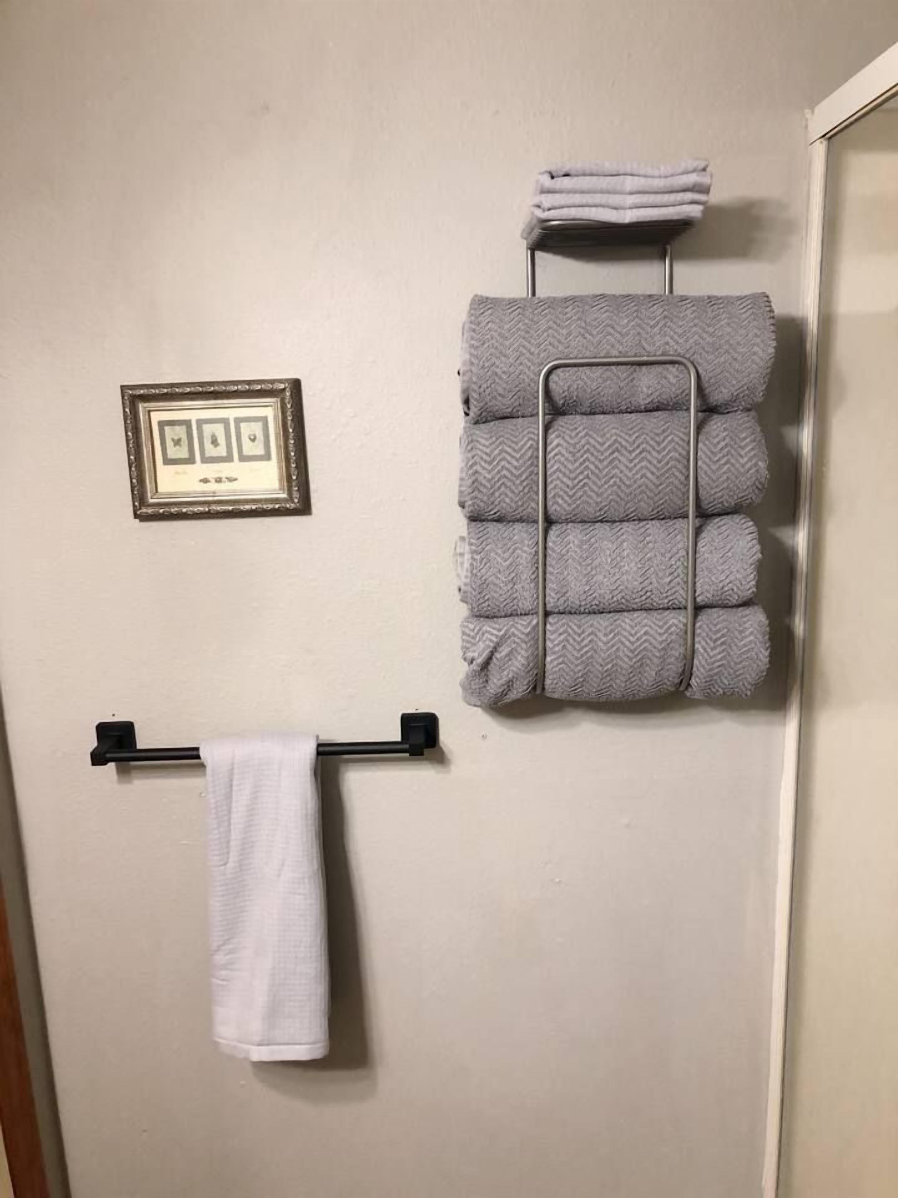 A bathroom with a towel rack, a framed picture, and a stack of folded towels.