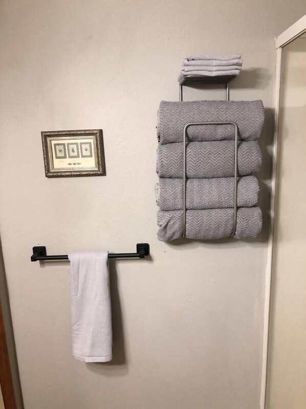 Een badkamer met een handdoekhouder, een lijst met een afbeelding en een stapel opgevouwen handdoeken.