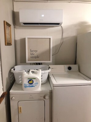 Een wasruimte met een wasmachine, droger en een wandairconditioner.
