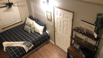 Une chambre à coucher avec un lit, une porte, une étagère avec des livres et des lunettes, et un ventilateur de plafond.
