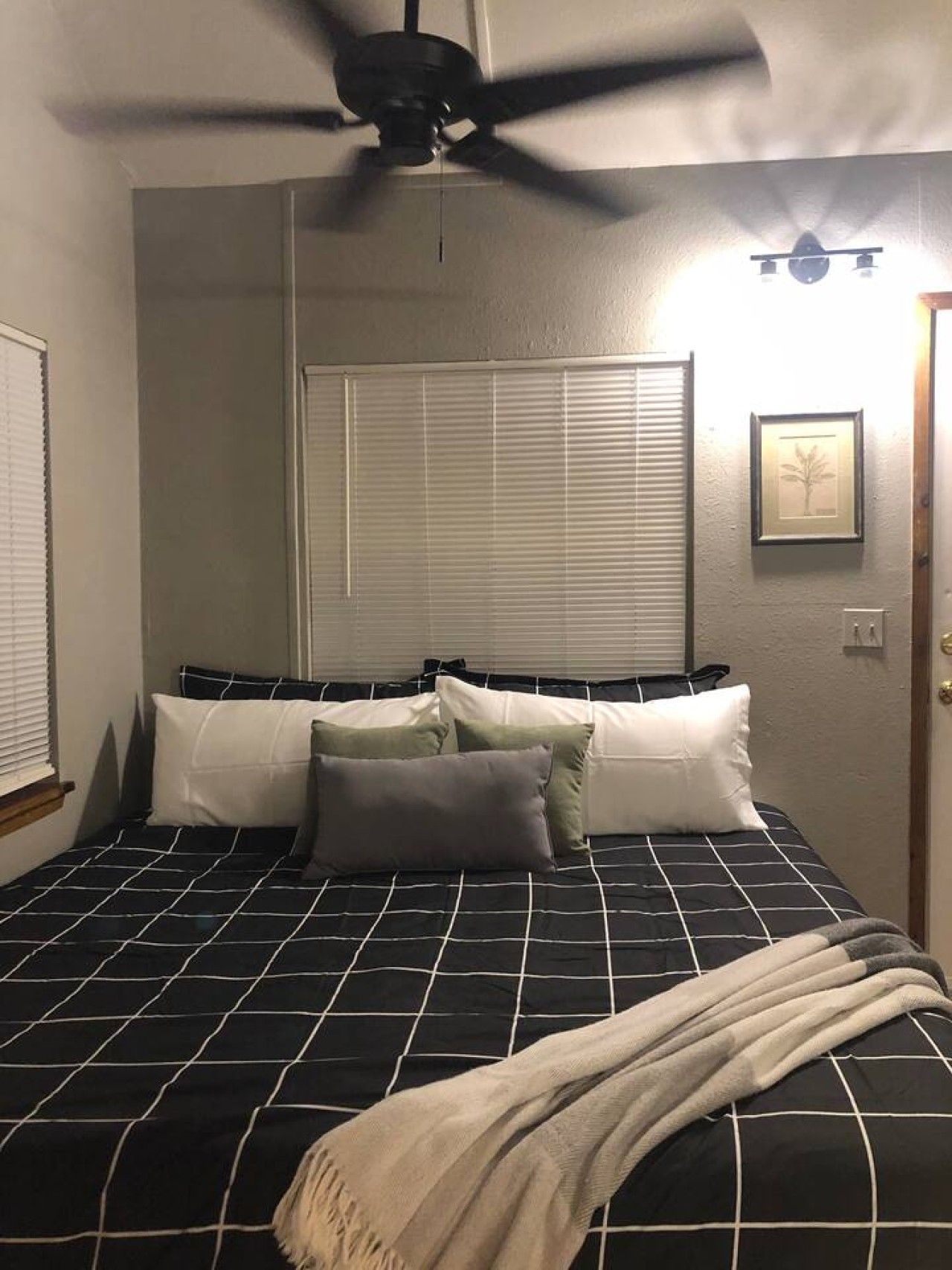 A bedroom with a bed, a ceiling fan, a window with blinds, and a door.