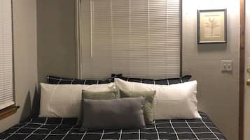 A bedroom with a bed, a ceiling fan, a window with blinds, and a door.